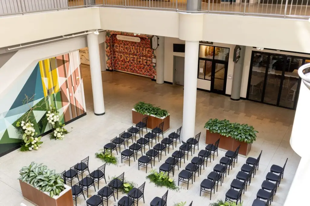 North Atrium at The Mercantile On Main set for a wedding ceremony, with rows of black chairs between planters and a colorful geometric mural, seen from the balcony above