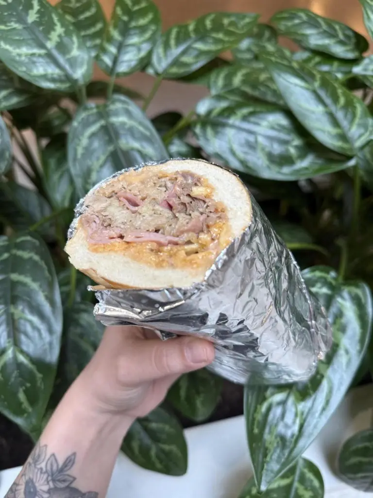 Foil-wrapped sandwich held in front of greenery