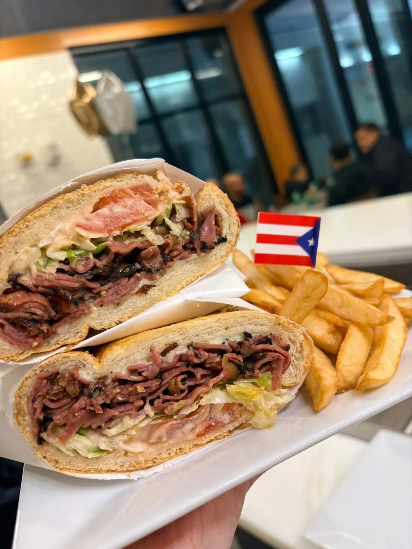 A tripleta sandwich and fries on a plate with a Puerto Rican flag pick at El Rey de las Tripletas Café